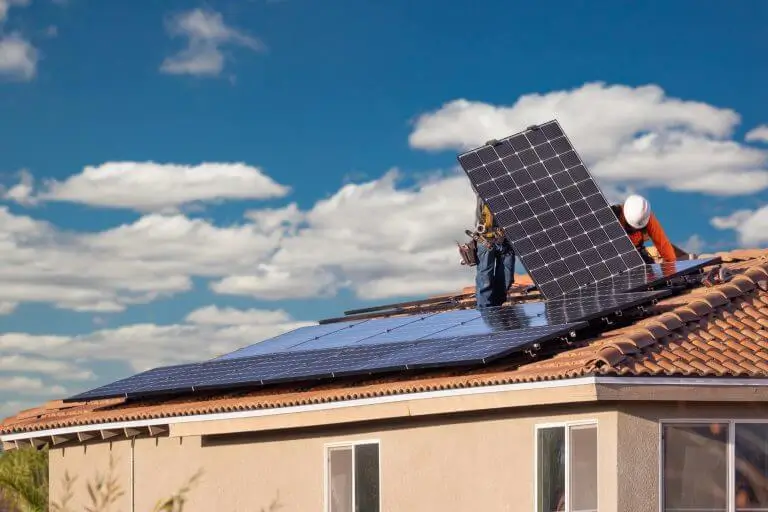 Two people holding a solar panel on it's side while installing it on the roof.