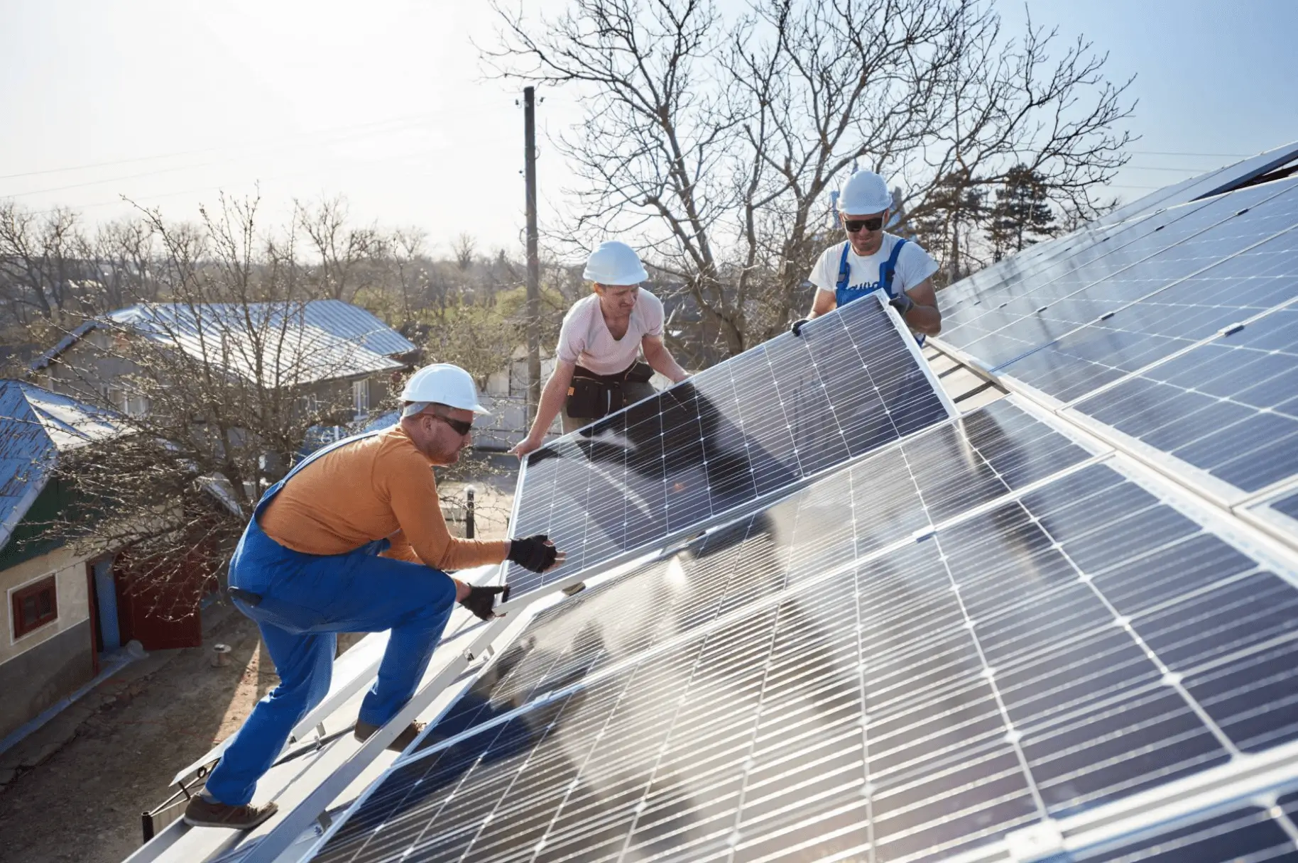 Three people holding and installing solar panels on a roof