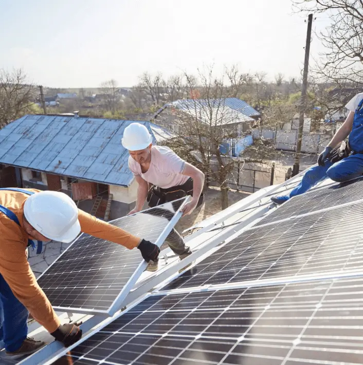 Two people holding a solar panel maneuvering it into place on roof