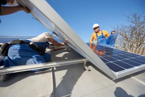 Two people installing solar panels on a metal roof