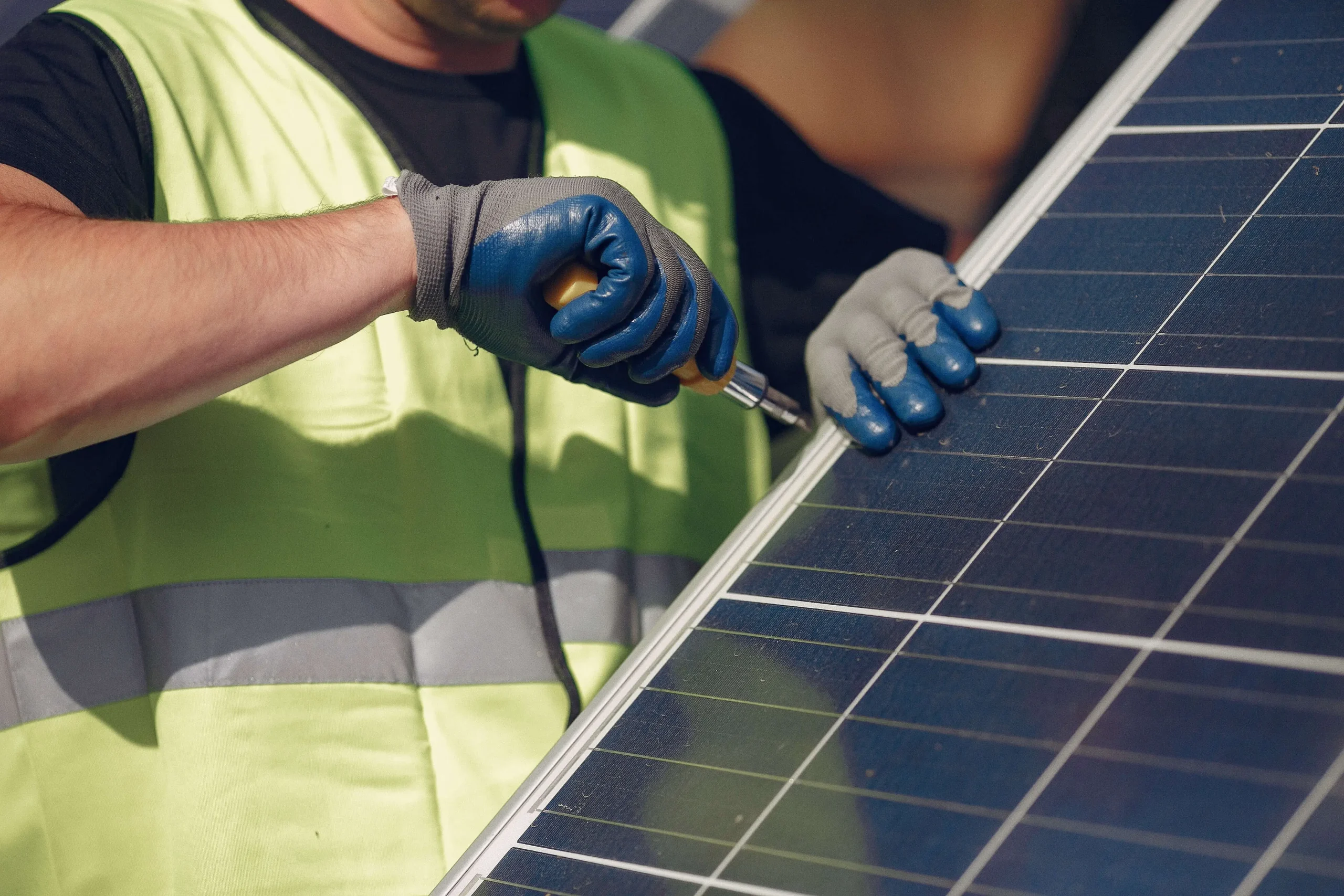 Close up of yellow vested person with screwdriver on side of solar panel