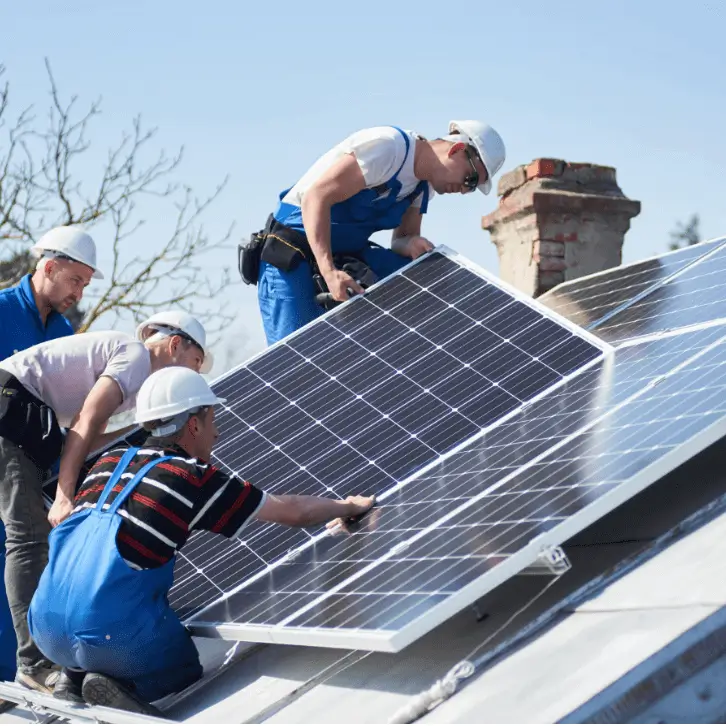 Four people installing and holding solar panels on a roof with chimney in background