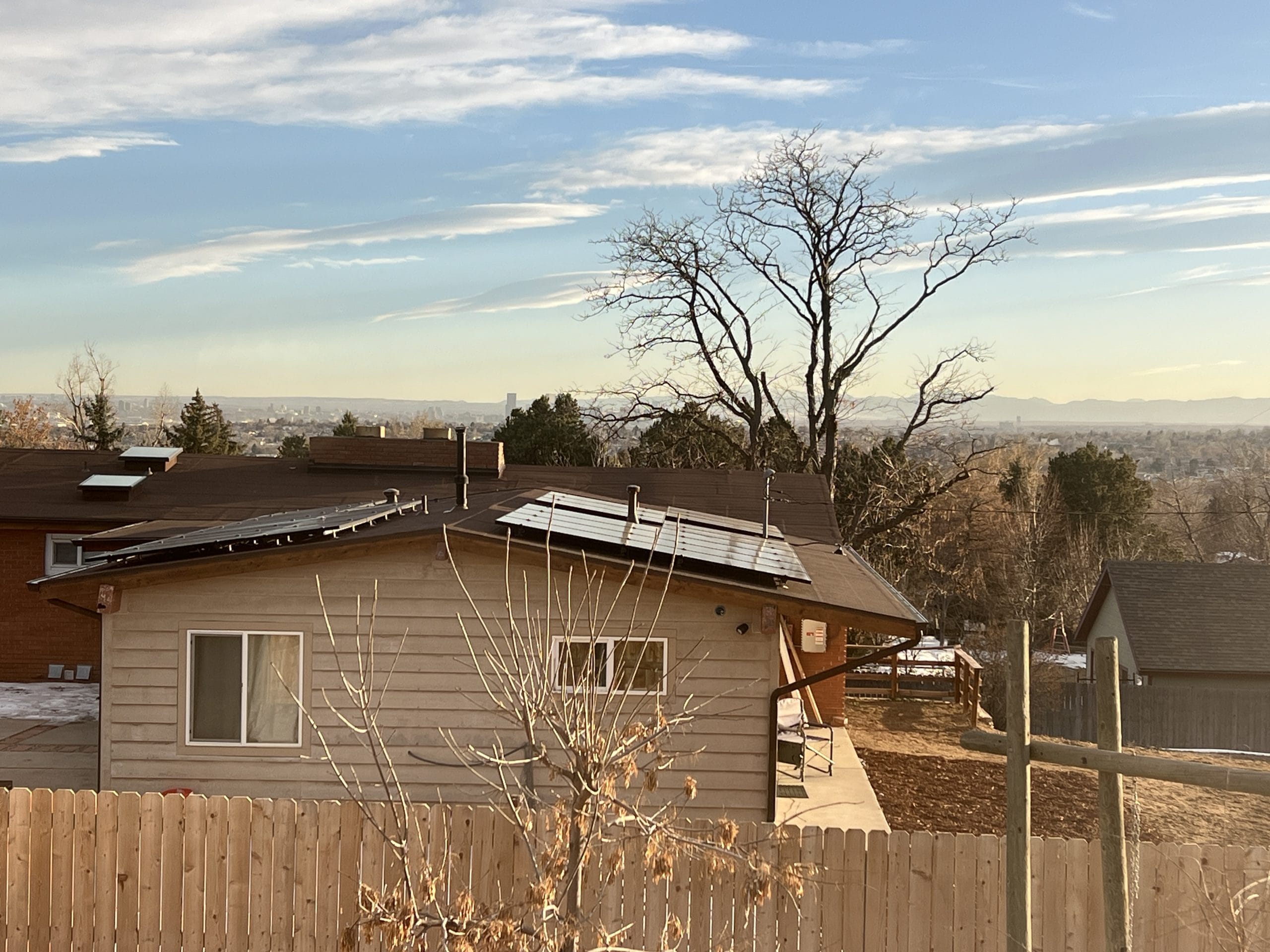 Tan house with solar panels on the roof, above view with sunset over Denver in the background.