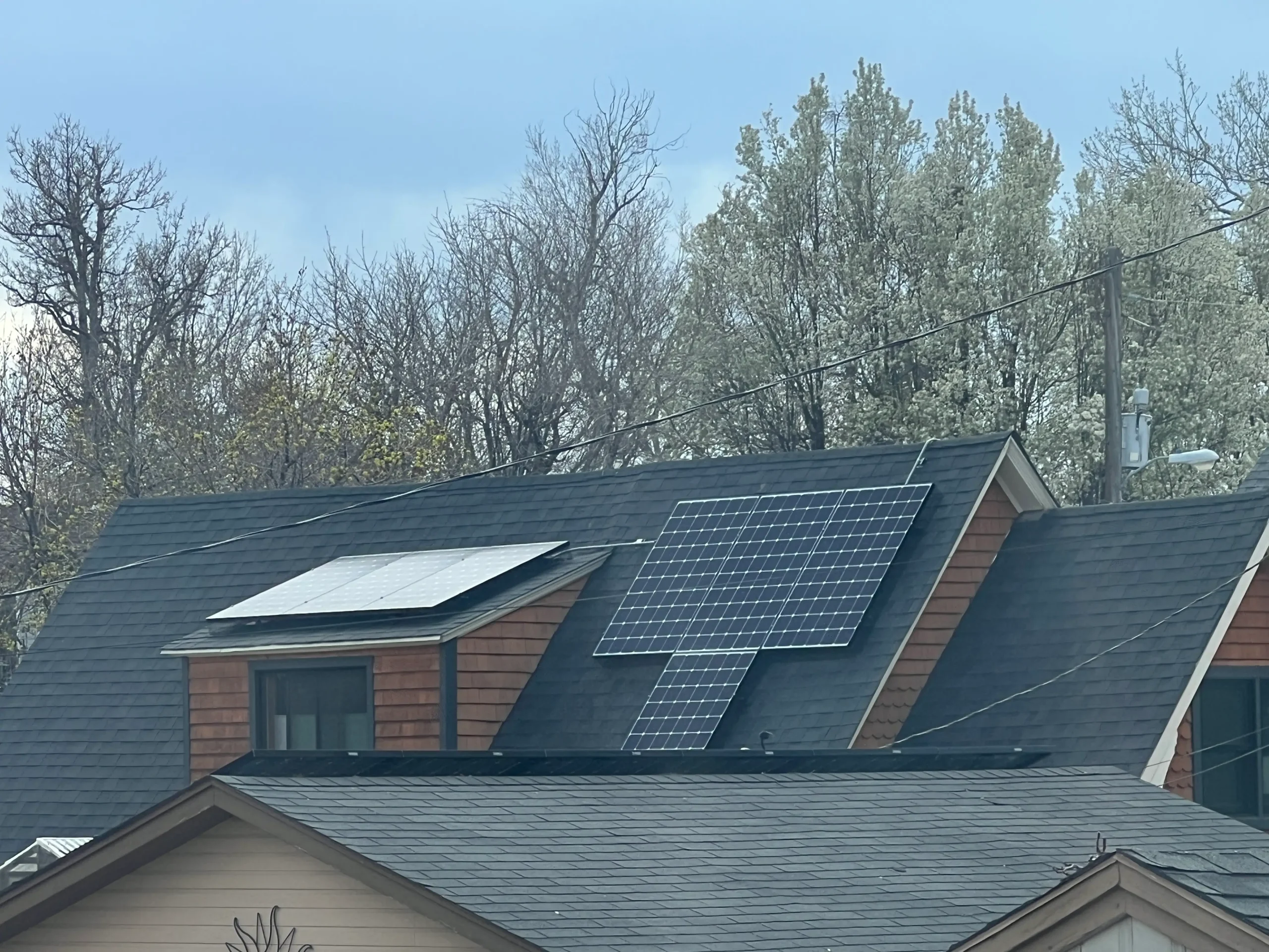 Close up of a rood with 7 solar panels on black roof in Denver with trees in the background.