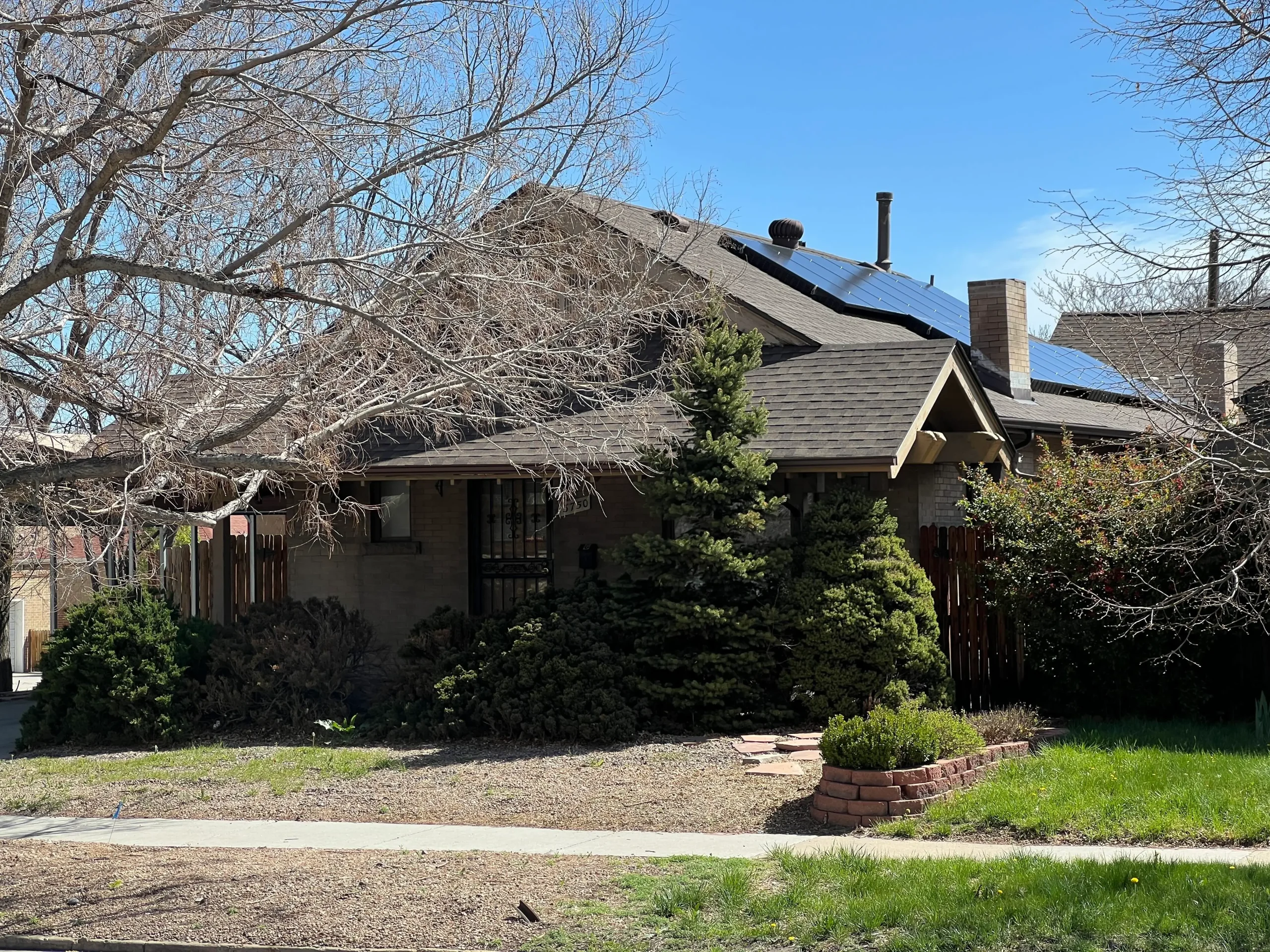 Vies of the front of a house with solar panels on the side of the roof, with some winter trees in the front.