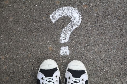 A question mark in chalk on outside pavement with some converse shoes in front of it like looking down and standing above the question mark. 